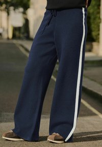Navy leveled legs -housut, jotka on valmistettu pehmeästä kankaasta ja joissa on valkoinen sivuraita sekä säädettävä kiristysvyötärö. Kontrastinväriset kengät mukana.