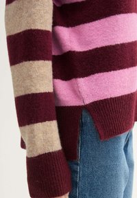 Gestreifter Pullover in Burgunderrot, Rosa und Beige, aus einem weichen, texturierten Material; mit seitlichen Schlitzen und gerippten Bündchen für zusätzliche Details.