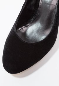 Escarpin en velours noir avec un bout arrondi et un intérieur lisse et brillant. Présente un design dégagé et une couture délicate le long du bord.