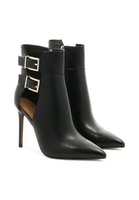 Botas de cuero negras hasta el tobillo con punteras puntiagudas, hebillas de hardware dorado a los lados y tacones altos y delgados. Textura suave y diseño elegante.