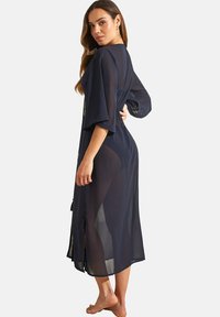 Robe en kimono transparent de couleur marine avec des manches larges, des fentes sur les côtés et un dos ouvert, ornée de délicieuses broderies florales au niveau du col.