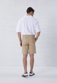 White polo shirt, beige shorts, and black-and-white sneakers. Shorts feature a classic fit, with back pockets and a smooth texture.