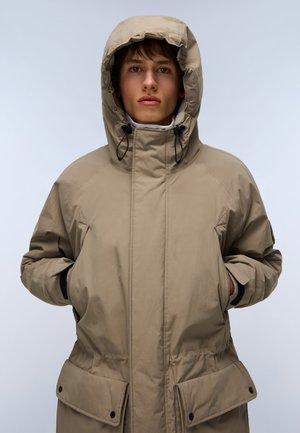 Beige isolerad parka med stor huva, framfickor och justerbara dragsnören. Slät textur och praktisk design för värme.