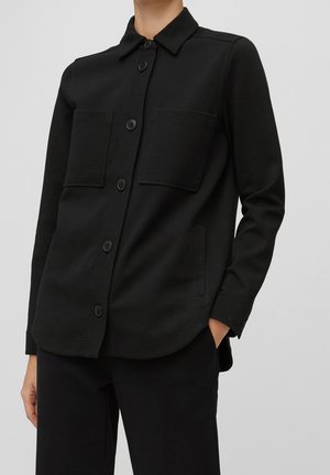 Musta napillinen takki, joka on valmistettu sileästä kankaasta ja jossa on kaksi rintataskua, kaulus sekä pitkät hihat napillisilla hihoilla.