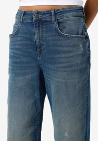 Blauwe denim jeans met een relaxte pasvorm, voorzien van een vervaagde was, vijf zakken en versleten details aan de voorkant.