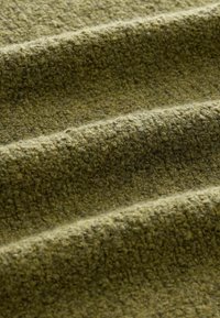 Textured green fabric with a soft, woven appearance; features folds and a blend of light and dark green fibers.