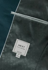 Slim-fit jacka inuti i mörk teal med ett mönstrat grått foder. Har en etikett som säger "NEXT TAILORING SLIM FIT 40R."