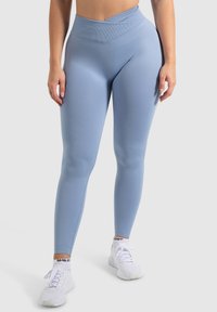 Leggings azzurro chiaro a vita alta realizzati in un tessuto morbido e elastico, con una vita a coste e un design aderente. Indossati con sneakers bianche.
