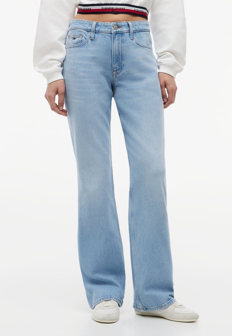 Jean large taille haute bleu clair porté avec des baskets blanches et un sweat court blanc montrant une ceinture de marque.