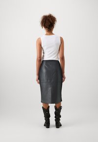 Jupe crayon en cuir noir avec des coutures verticales, associée à un haut sans manches blanc. Longueur genou avec une texture lisse, se tenant avec des bottes noires jusqu'aux genoux.