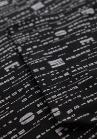 Černá látka s vzorem různých bílých textů a symbolů, s měkkou texturou a mírně skládovým vzhledem.