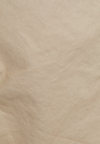 Tissu beige avec une texture lisse et un motif tissé fin, affichant des variations subtiles de teinte à la surface.