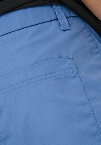 Pantaloni shorts azzurri chiari realizzati in tessuto liscio. Le caratteristiche includono una tasca piatta e una cucitura pulita lungo la vita, con hardware visibile minimale.