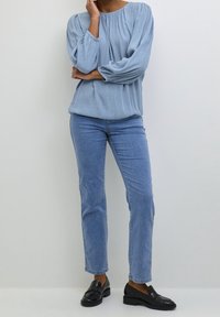 Blouse texturée bleu clair avec des manches ballon, assortie à un jean droit bleu clair et des mocassins noirs. Tenue simple et décontractée.