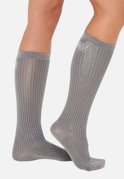 Knee-high sokid heledas hallis värvitos, vertikaalse ribavaluga tekstuuriga ja siledas, pehme viimistlusega. Üleval on tugevdatud äär.