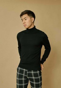 Pull noir à col roulé en tissu doux, associé à un pantalon à carreaux noir et blanc. Texture lisse et design ajusté sans embellissements.