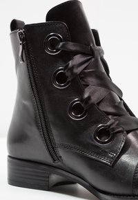 Bottine en cuir noir avec fermeture éclair latérale, devant à lacets en satin, œillets en métal et talon plat à finition texturée.