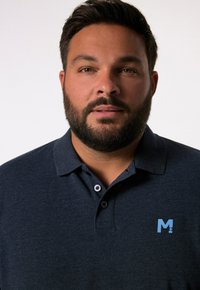 Tmavě modré polo tričko s krátkým rukávem, dvěma knoflíky a světle modrým logem na levé hrudi. Hladká textura. Jednoduchý design.