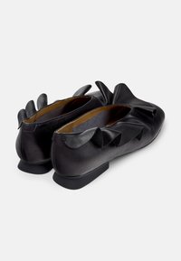 Zwarte leren ballerina's met een lage hak, voorzien van decoratieve verhoogde accenten aan de achterkant. De binnenkant heeft een zachte voering en een gladde textuur.