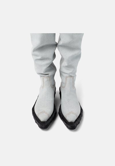Botines de tela gris con una suela negra texturizada, con costuras visibles y un diseño elegante, que se estrechan hacia los dedos.