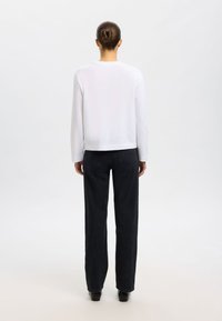 Weißes Langarmshirt und schwarze, hoch taillierte Jeans mit lockerem Schnitt, glattem Stoff und einfachen Nähdetails.