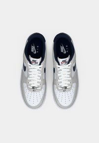 Nike Air Force 1 tenisice s bijelim kožnim prednjim dijelom, gornjim dijelom od sivoj antilop kože, mornarsko plavim naglascima, okruglim vezicama i perforiranim detaljima na prstima.