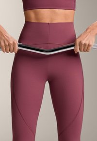 Mani che afferrano una barra metallica piegata all'altezza della vita, con una persona che indossa leggings da allenamento mauve a vita alta e un reggiseno sportivo abbinato.