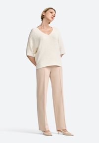 Pull en maille texturée blanc, oversize, avec un col en V, associé à un pantalon beige ajusté et des escarpins nude à bout pointu. Design simple et moderne.