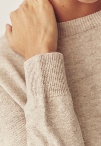 Jasnobeżowy sweter dzianinowy z prążkowanymi mankietami i gładką fakturą, z zbliżeniem ukazującym miękkość tkaniny.