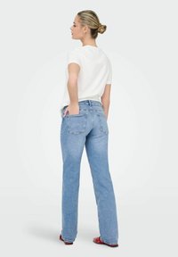 Svijetloplava traperica klasičnog ravnog kroja, s pet džepova i suptilnim detaljima prošivanja, u kombinaciji s bijelom majicom.