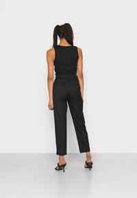 Svart ärmlös topp som är kombinerad med högmidjade svarta byxor. Byxorna har en texturerad midjeband och sidofickor. Modellen har på sig svarta klackar.