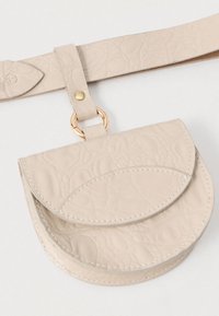 Torbica u boji kreme od kože s teksturiranim cvjetnim uzorkom, okruglog oblika, s zlatnim metalnim prstenom. Priložena naramenica za nošenje.