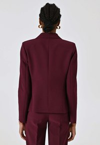 Blazer bordeaux con vestibilità sartoriale, realizzato in tessuto elegante. Caratterizzato da un colletto con rever ad intaglio e linee pulite, abbinato a pantaloni coordinati.
