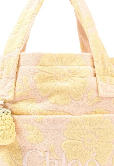 Borsa a tracolla in tessuto morbido con motivo floreale giallo pallido, manici larghi e un piccolo portachiavi all'uncinetto attaccato a un lato.