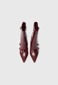 Burgundy ankelstøvler med en blank læderfinish, spidse tæer og sidelukninger. Dekorative metaldele på siden.