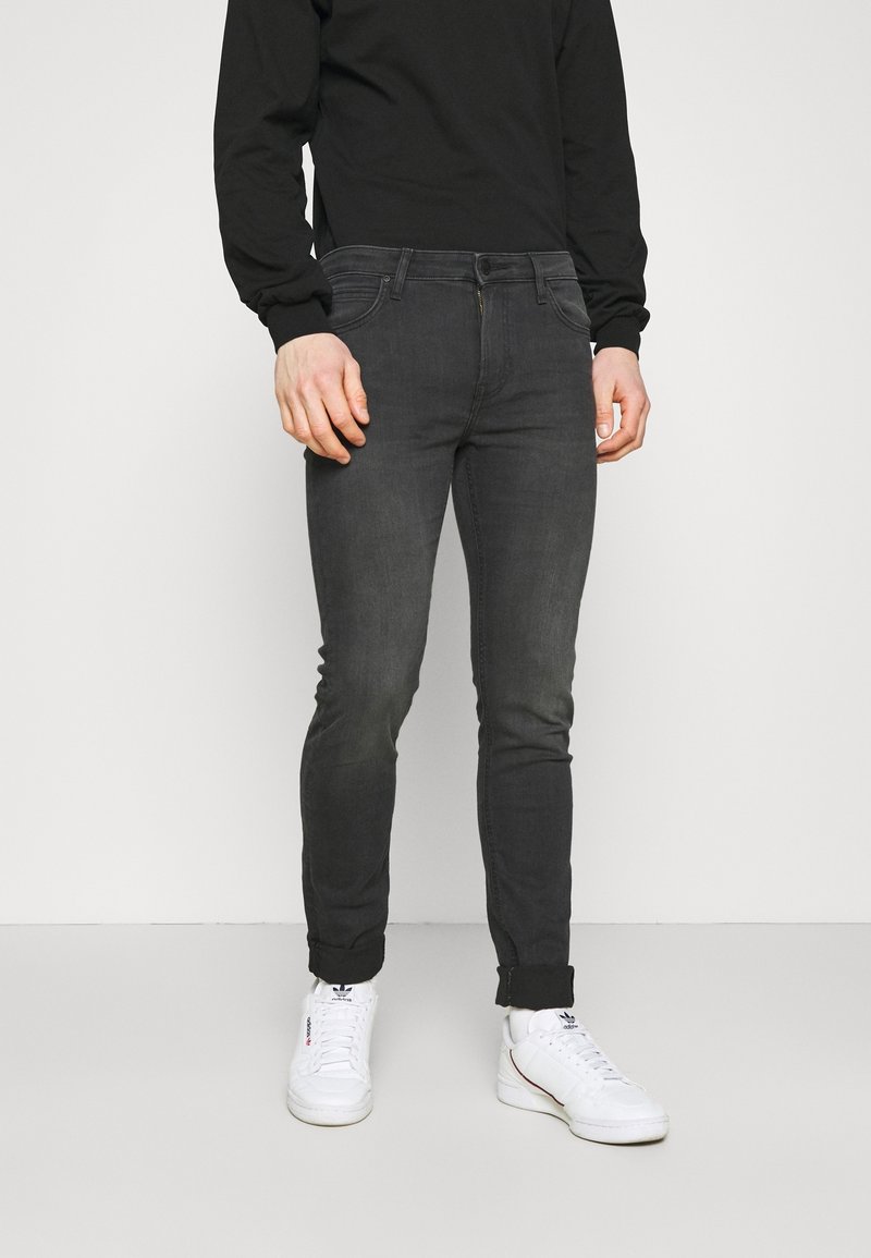 Svarta skinny jeans med en blekt finish, fem fickor, och stängning med knapp och blixtlås, kombinerade med vita sneakers.