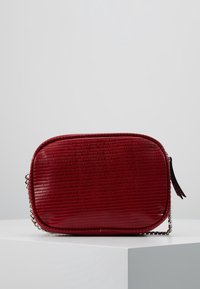 Borsa rettangolare rossa con superficie strutturata, con tracolla in catena argentata e chiusura a zip. Presenta una finitura lucida e bordi arrotondati.
