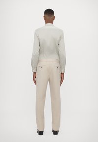Camicia a maniche lunghe grigia chiaro con polsini abbottonati, abbinata a pantaloni eleganti beige dal taglio slim e tasche posteriori, vista da dietro.
