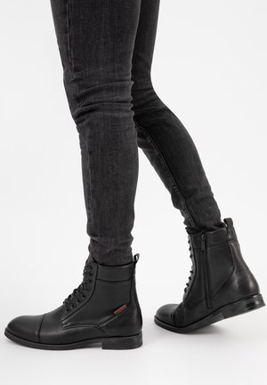 Zwarte leren enkelboots met veters en een zijrits, met een ronde neus en een lage, gestructureerde hak. Gemaakt in combinatie met slim-fit donkere jeans.