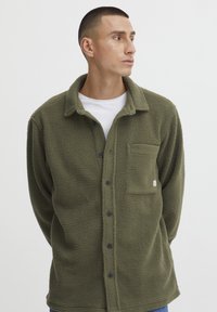 Olivengrønn fleece skjortejakke med en myk tekstur, knappelukking, krage og en brystlomme med en liten logo.
