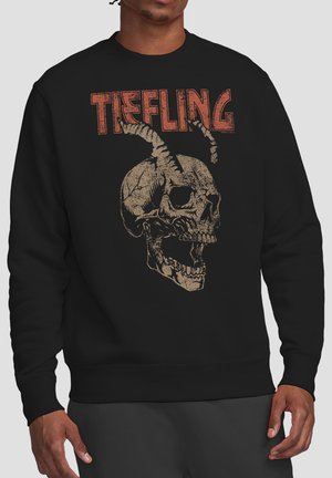 Person trägt einen schwarzen Sweatshirt mit einem detaillierten Schädel mit gedrehten Hörnern und dem Wort „TIEFLING“ in großen roten Buchstaben darüber.