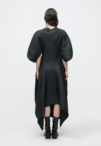 Μαύρο φόρεμα με φουσκωτά μανίκια, ασύμμετρο τελείωμα, υφασμάτινη υφή και κρυφό φερμουάρ στο πίσω μέρος. Συνδυασμένο με μαύρες μπότες μέχρι το γόνατο.