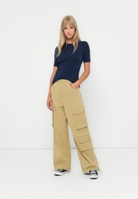 Marinblå kortärmad topp ihop med beige vida cargobyxor med stora fickor. Skorna består av svartvita sneakers.