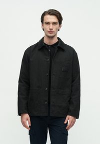 Μαύρο μπουφάν με γιακά από κοτλέ, κλείσιμο με κουμπιά, δύο μπροστινές τσέπες και μια τσέπη με επιφάνεια στο αρι στερό στήθος. Υλικό από βαμβάκι.