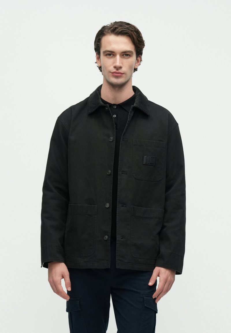 Μαύρο μπουφάν με γιακά από κοτλέ, κλείσιμο με κουμπιά, δύο μπροστινές τσέπες και μια τσέπη με επιφάνεια στο αριστερό στήθος. Υλικό από βαμβάκι.