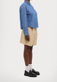 Jeansskjorta med knappar, korta ärmar, ljusblå. Bruna shorts och svarta platåskor med vita strumpor. Klara linjer, avslappnad stil.