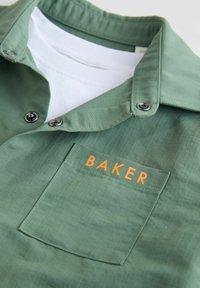 Zelená texturovaná košile s límcem, patentními knoflíky a náprsní kapsou, na které je v oranžovém písmu nápis "BAKER".