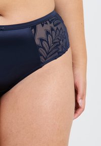 Mutandine alta in vita colore blu navy, con una parte frontale liscia e pannelli laterali in pizzo trasparente con un motivo a foglie. Texture morbida, vita elastica.