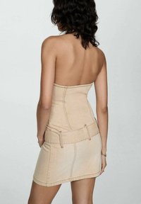 Robe mini sans manches en denim beige avec un corsage ajusté et une jupe courte, présentant des coutures visibles et des passants de ceinture. Texture lisse.