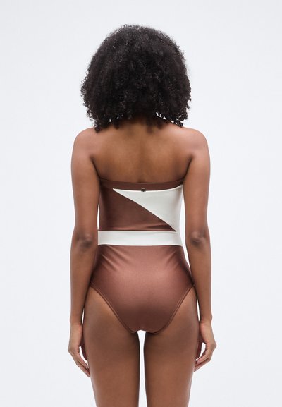 Barna és fehér színű, pánt nélküli fürdőruha, magasított derekú alsó résszel és háromszög alakú kivágásokkal, sima, fényes textúrával.